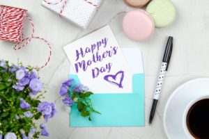 happy mothers day card beside pen macaroons flowers and box 2072160